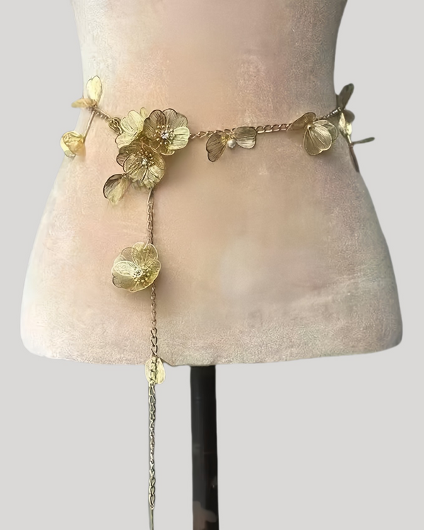 Gold metal floral waist chain displayed on a pink velvet form