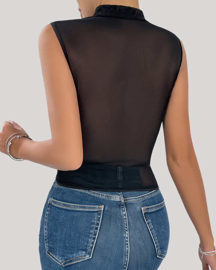 Person wearing a black sheer top and blue jeans on a plain background