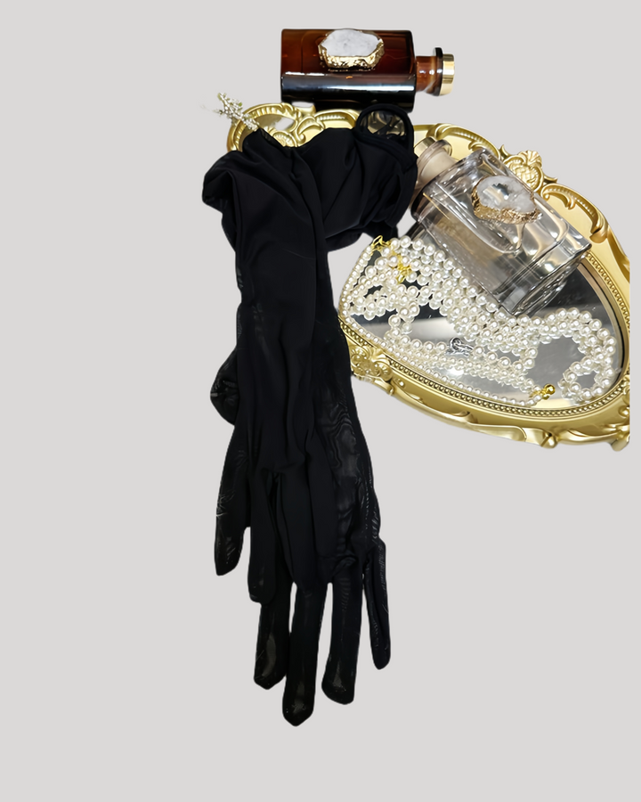 Black gloves and a decorative perfume bottle with a gold heart-shaped stand on a light gray background