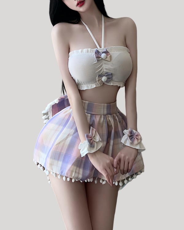 Woman wearing a pastel plaid bunny costume set, featuring a white bandeau top with pom-pom bows, a pleated mini skirt trimmed with white pom-pom fringe, matching plaid bunny ears headband, and ruffled wrist cuffs.