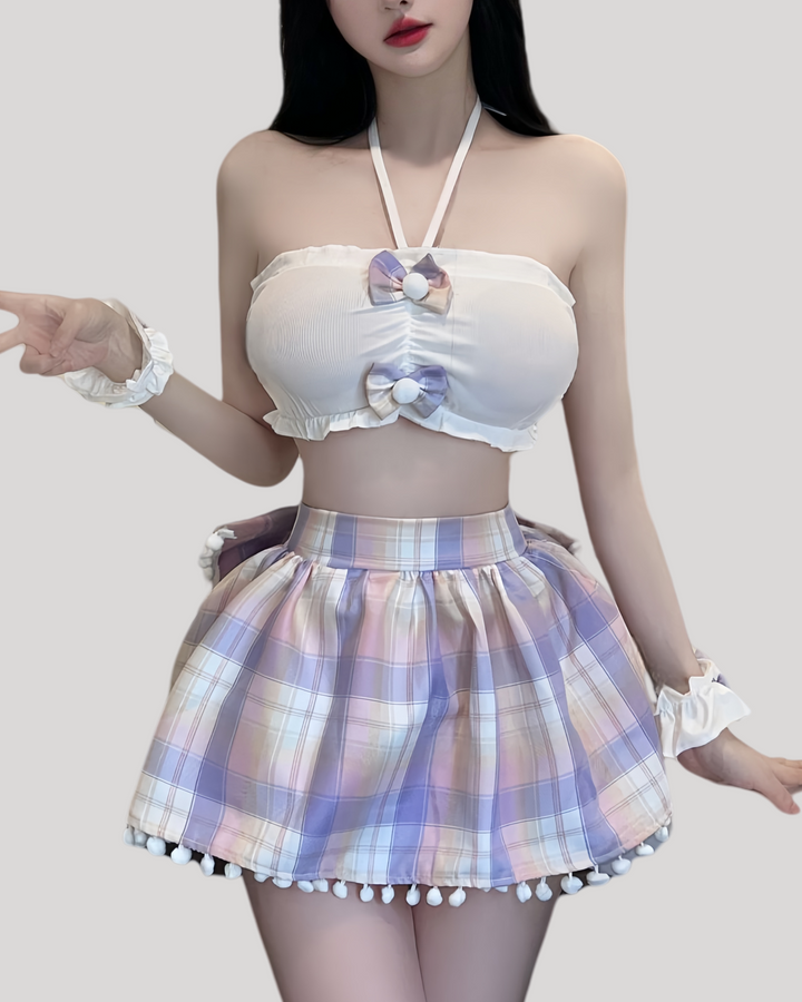 Woman wearing a pastel plaid bunny costume set, featuring a white bandeau top with pom-pom bows, a pleated mini skirt trimmed with white pom-pom fringe, matching plaid bunny ears headband, and ruffled wrist cuffs.