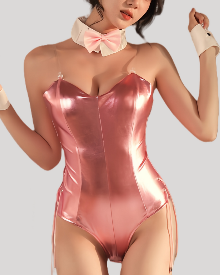 Model wearing a pink patent leather bunny bodysuit with attached tail, clear shoulder straps, matching black bunny ears headband, white collar with black bow tie, and cuff wristbands.