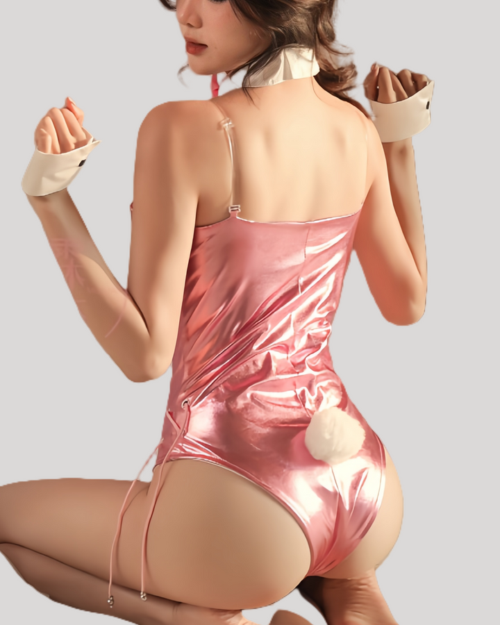 Model wearing a pink patent leather bunny bodysuit with attached tail, clear shoulder straps, matching black bunny ears headband, white collar with black bow tie, and cuff wristbands.