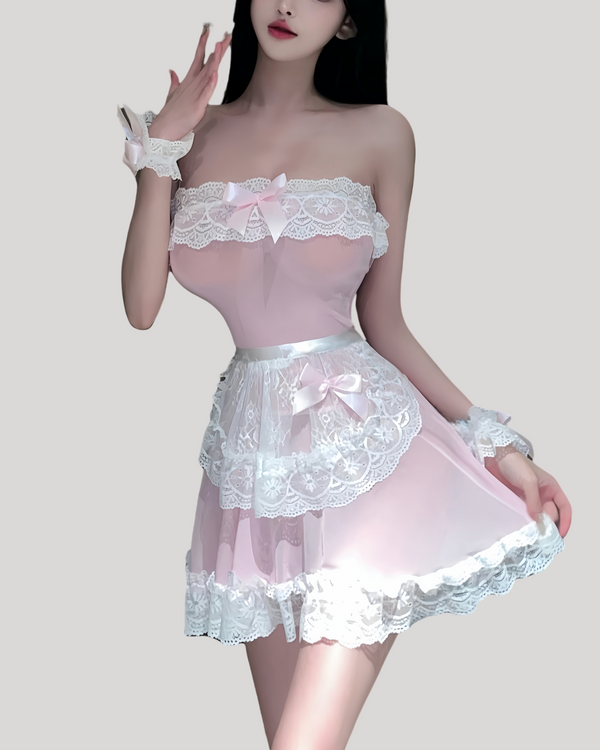 Model in a strapless pink sheer maid dress with white lace trim, matching lace apron, ruffled wrist cuffs, and lace headband in a modern hotel room setting