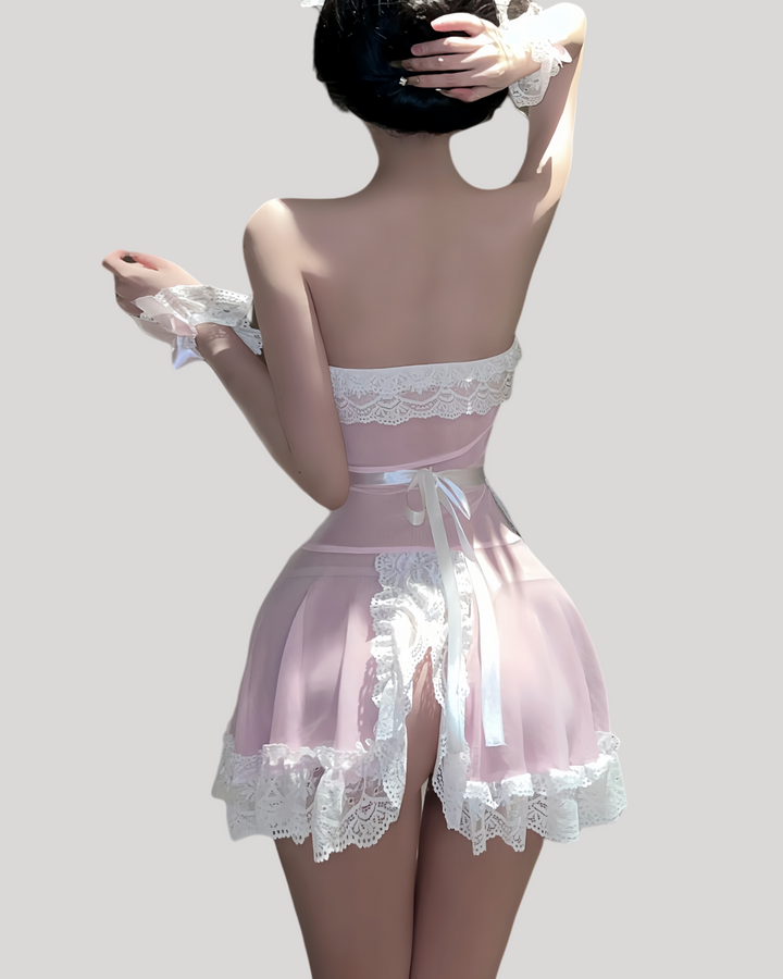 Model in a strapless pink sheer maid dress with white lace trim, matching lace apron, ruffled wrist cuffs, and lace headband in a modern hotel room setting