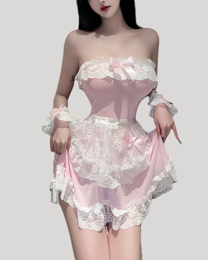 Model in a strapless pink sheer maid dress with white lace trim, matching lace apron, ruffled wrist cuffs, and lace headband in a modern hotel room setting