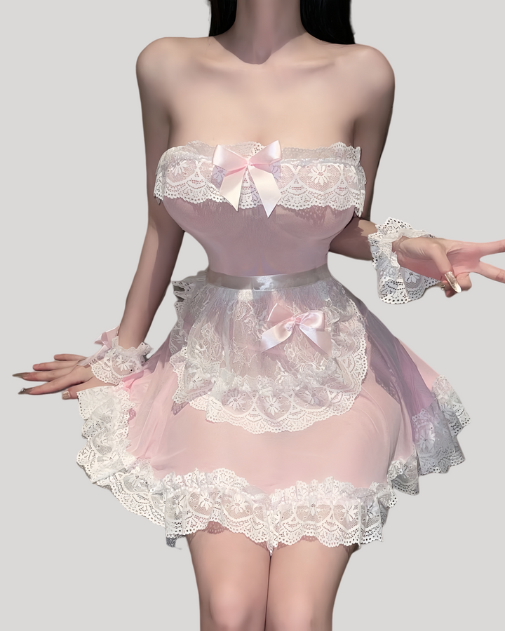 Model in a strapless pink sheer maid dress with white lace trim, matching lace apron, ruffled wrist cuffs, and lace headband in a modern hotel room setting