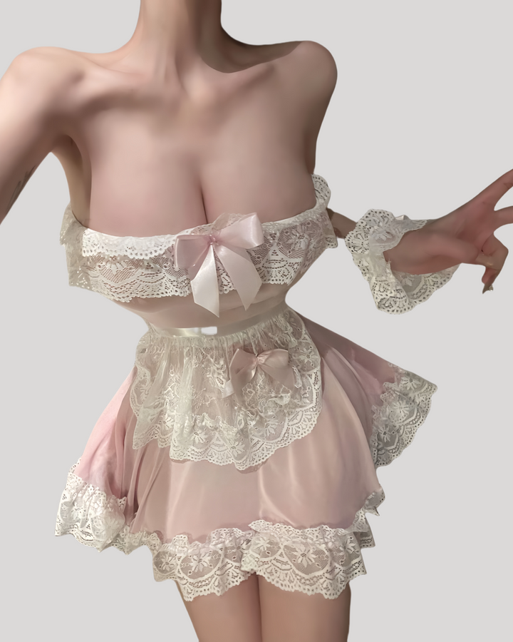 Model in a strapless pink sheer maid dress with white lace trim, matching lace apron, ruffled wrist cuffs, and lace headband in a modern hotel room setting