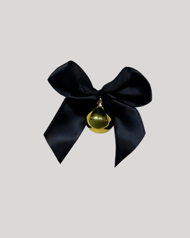 Flat lay of lace choker with black bow and bell on white fabric