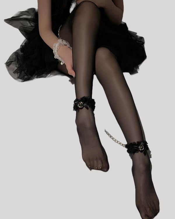Model wearing black bell anklet cuffs with chain connection on bed